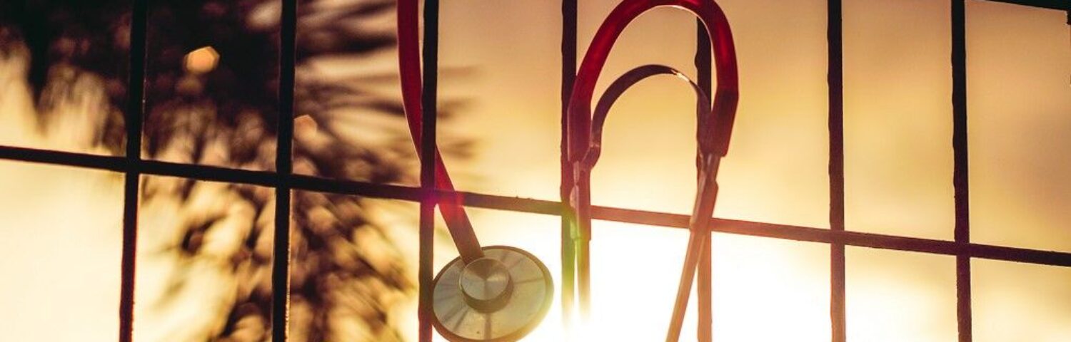 Photo d'un stéthoscope suspendu à une grille, un coucher de soleil derrière